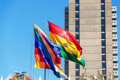 Low angle view of wiphala and bolivian flags against building