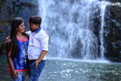 Young couple standing against waterfall at river