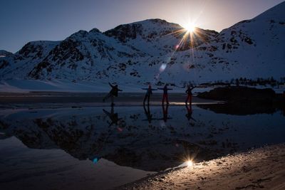 Silhouette people by lake against snowcapped mountains and sky