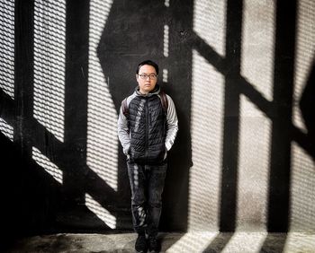 Portrait of young man standing against shadow patterned wall.