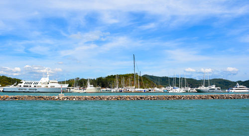 Sailboats moored at harbor against blue sky