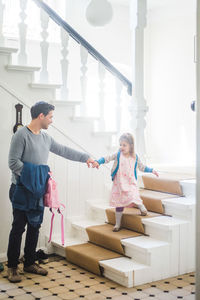 Full length of father holding schoolgirl moving down steps at home