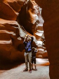 Father and son photographing while standing by rock formation