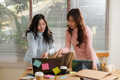Smiling friends using mobile phone while sitting in cafe