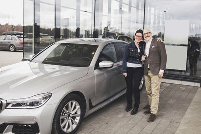 Portrait of senior couple standing by car against showroom