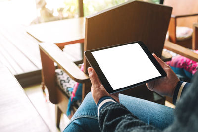 Cropped hands of woman using blank digital tablet in cafe