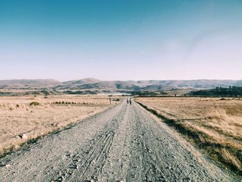 People on dirt road amidst landscape against sky