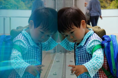 Cute boy in school uniform reflecting on glass wall