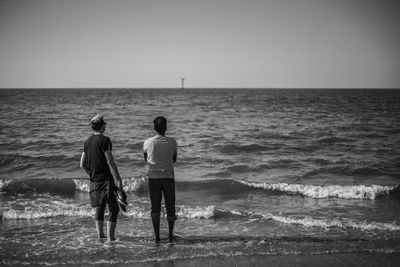 Rear view of men on beach against sky