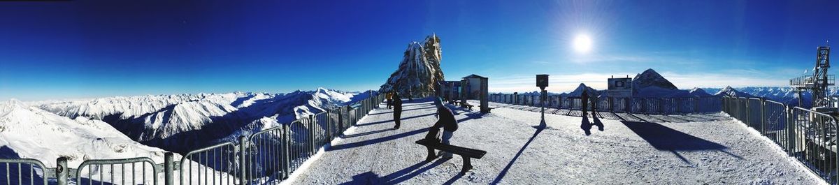 Panoramic view of people by snowcapped mountain against sky on sunny day