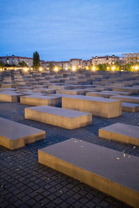 Illuminated city by street against sky at dusk