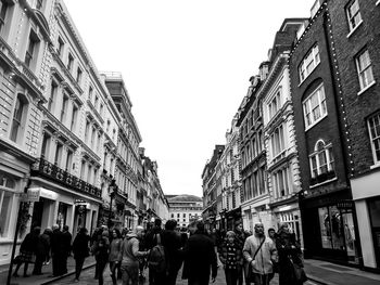People walking on street amidst buildings in city against sky