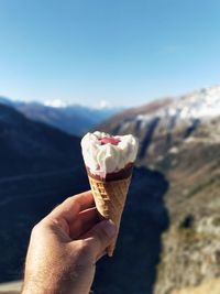 Cropped hand of man holding ice cream against mountain