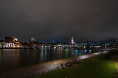 Illuminated city by river against sky at night