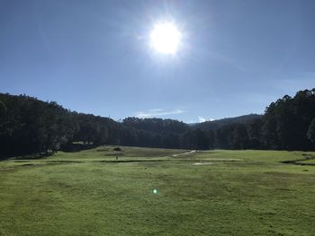 Scenic view of golf course against sky on sunny day