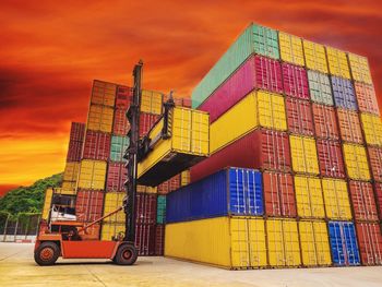 Vehicle stacking colorful cargo containers against orange sky