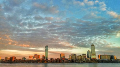 Sea by modern buildings against sky during sunset