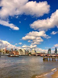View of buildings by river against cloudy sky