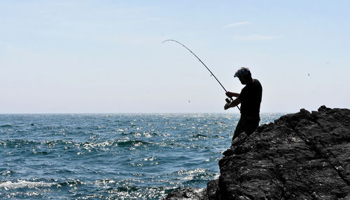 Side view of man fishing in sea against sky