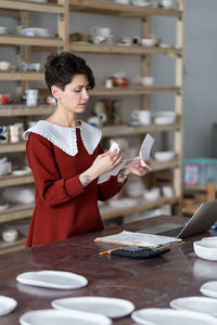 Young woman ceramic studio owner managing small business finances, doing pottery cost analysis