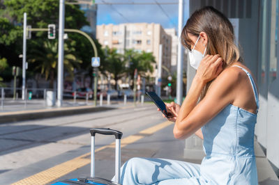 Woman using mobile phone while sitting in city