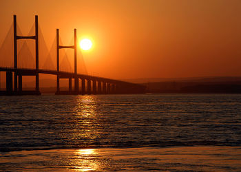 View of suspension bridge over sea at sunset