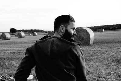 Rear view of man against hay bales on field against sky