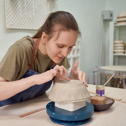 Concentrated young woman ceramist working on clay ware with satisfaction as recreation 