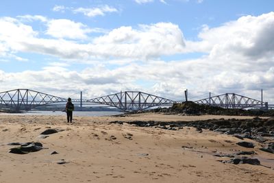 Person standing at beach against firth of forth rail bridge