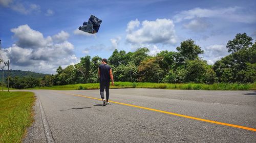 Rear view of man standing by road against sky