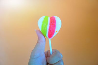 Close-up of hand holding heart shape against pink background