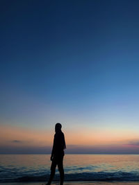 Silhouette woman standing at beach against blue sky during sunset