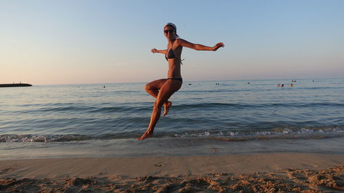 Young woman jumping on beach against clear sky