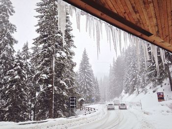 Low angle view of icicles on roof against cars on snowcapped road