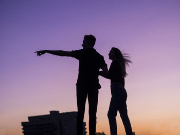 Silhouette man with woman gesturing against clear sky at sunset