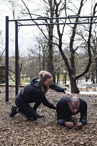 Side view of young woman assisting man to perform plank position in forest