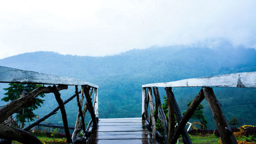 Wooden footbridge by mountains against sky