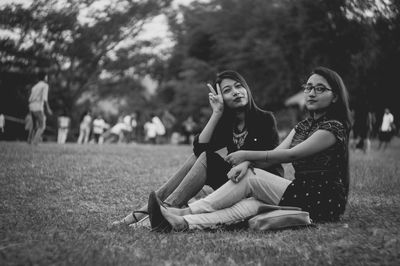 Young women sitting on grass against trees