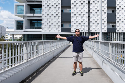 Full length portrait of smiling man standing on bridge in city
