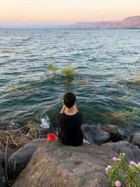 Rear view of woman sitting on rock against sea