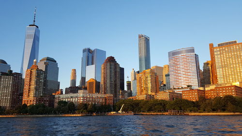 Low angle view of city skyline by river against clear sky