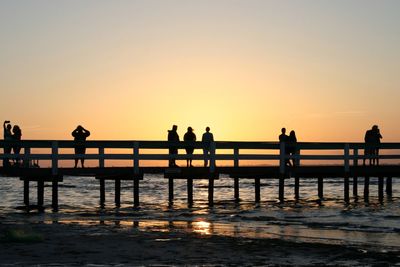 Silhouette people standing by railing against orange sky