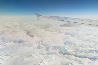 Aerial of alps covered with snow with airplane wing and blue sky