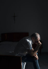 Side view of young man sitting on bed at home