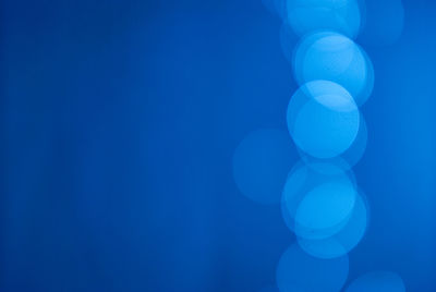 Close-up of illuminated defocused lights over blue background