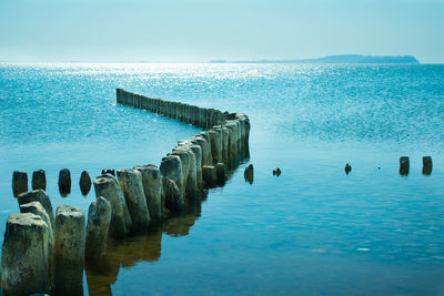 Wooden posts in sea against clear blue sky