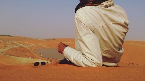 Low section of man on sand at beach against clear sky