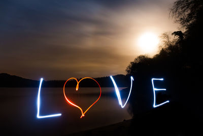 Close-up of illuminated text against sky at sunset