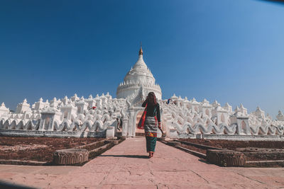 Rear view of man outside temple against blue sky