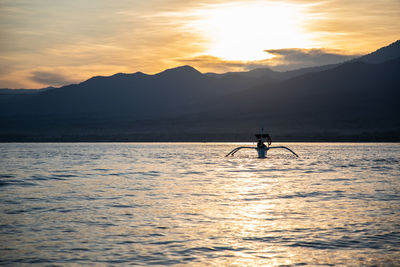 Silhouette person in sea against sky during sunset